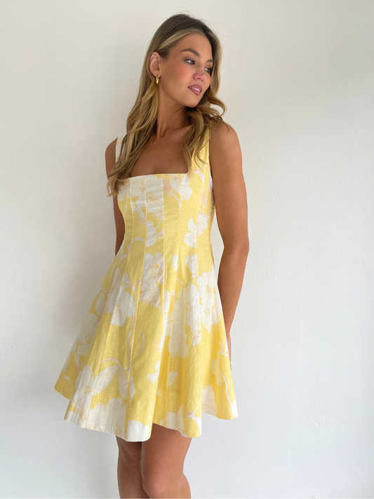 By Nicola Milly mini dress in amarilla flor yellow floral print in cotton linen with  straps and flowy hem, perfect for daytime events and summer occasions. Exclusive to Coco & Lola