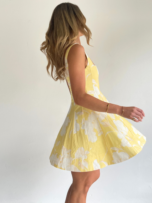By Nicola Milly mini dress in amarilla flor yellow floral print in cotton linen with  straps and flowy hem, perfect for daytime events and summer occasions. Exclusive to Coco & Lola