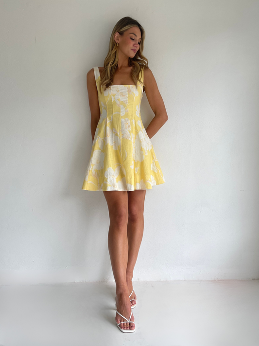 By Nicola Milly mini dress in amarilla flor yellow floral print in cotton linen with  straps and flowy hem, perfect for daytime events and summer occasions. Exclusive to Coco & Lola